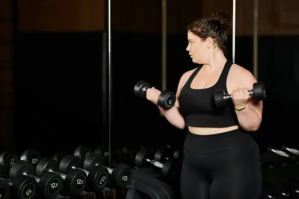 Una mujer de talla grande levanta pesas, mostrando fuerza y confianza en su rutina de entrenamiento. - foto de stock