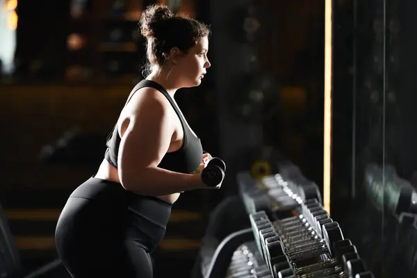 Eine Plus-Size-Frau umarmt ihre Stärke beim Training in einer lebendigen Fitnessstudio-Atmosphäre. — Stockfoto