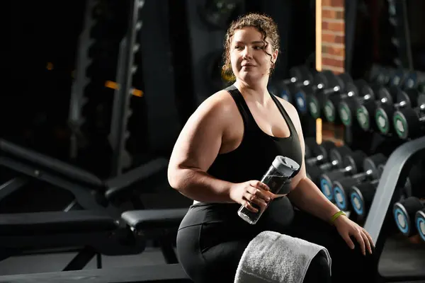Una joven confiada en ropa deportiva se toma un descanso durante su entrenamiento, abrazando la positividad corporal en el gimnasio. - foto de stock