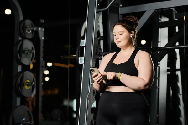 A confident young woman checks her phone while embracing a body positive workout in activewear. — Stock Photo