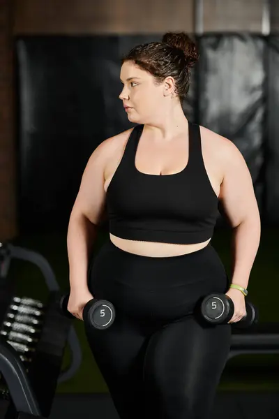 Eine selbstbewusste Frau stemmt Gewichte in stylischer Aktivkleidung und zeigt Stärke und Entschlossenheit im Training. — Stockfoto