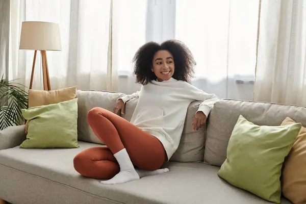 A young woman lounges comfortably in her living room, radiating warmth and relaxation in loungewear. — Stock Photo