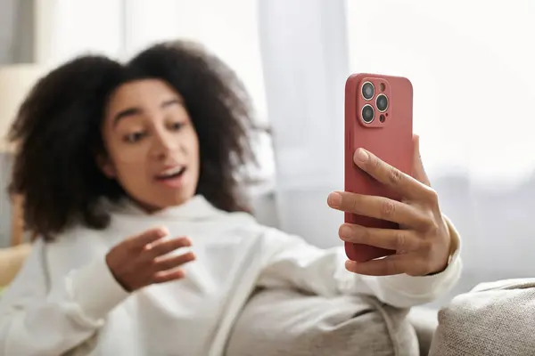 A young woman in a cozy outfit laughs while engaged in a video call from her living room. — Stock Photo