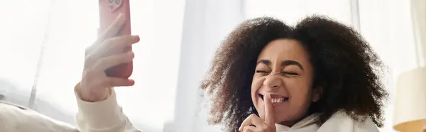 A cheerful young woman in cozy attire captures a fun moment while relaxing indoors. — Stock Photo