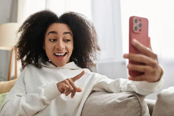 A young woman shares laughter and joy while connecting with friends from her cozy living room. — Stock Photo