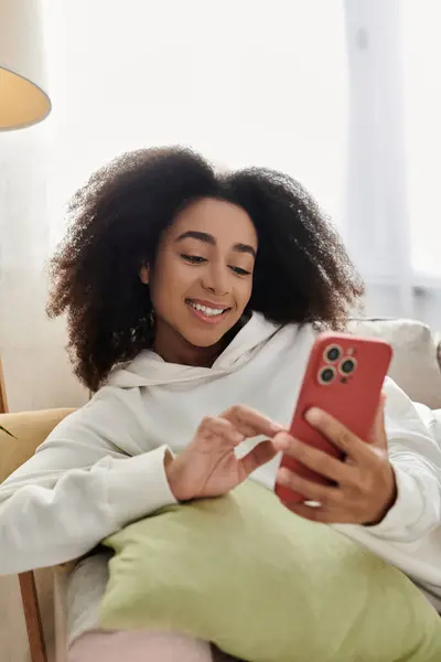 A young woman relaxes in her living room, engaged with her phone while wrapped in warmth. — Stock Photo