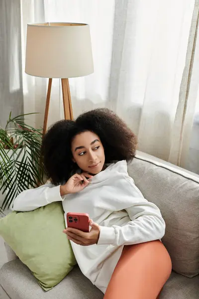 A young woman enjoys her time at home, comfortably browsing on her phone while lounging on the couch. — Stock Photo