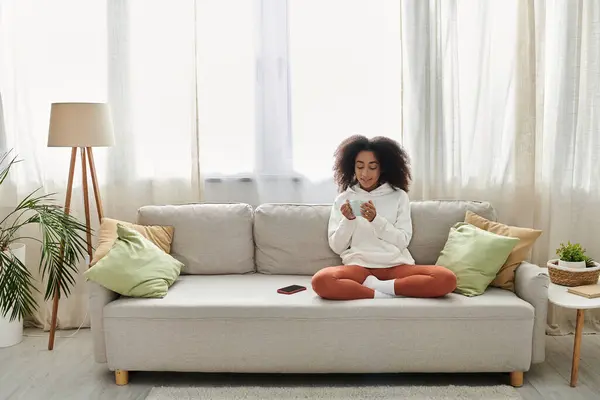 A young woman relaxes in her cozy living room, wearing a hoodie, leggings, and enjoying her time. — Stock Photo