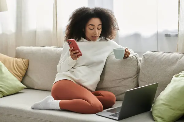 Eine junge Frau entspannt sich in ihrem gemütlichen Wohnzimmer und genießt Tee, während sie auf ihrem Laptop surft. — Stockfoto