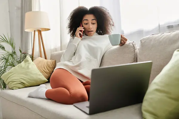 Uma jovem relaxa em sua sala de estar, tomando chá enquanto está envolvida em uma conversa telefônica. — Fotografia de Stock