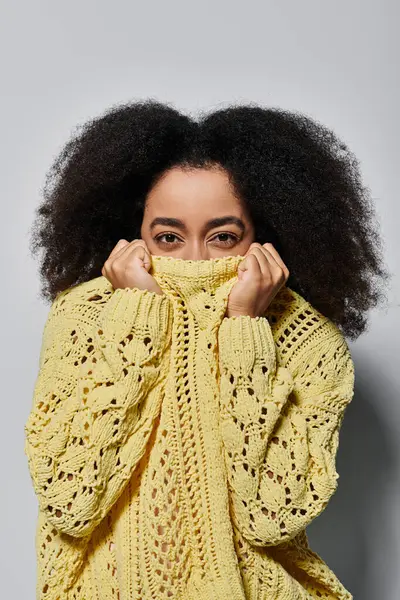 Eine junge Frau mit lockigem Haar versteckt ihr Gesicht spielerisch in einem leuchtend gelben Pullover. — Stockfoto