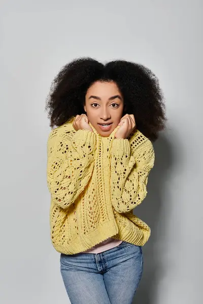 A young African American woman playfully poses in a bright yellow sweater, radiating warmth and joy. — Stock Photo