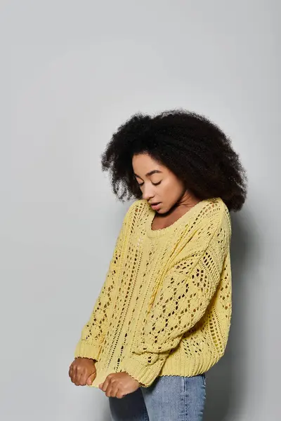 A young woman with curly hair showcases her style in a cozy yellow sweater, lost in thought. — Stock Photo