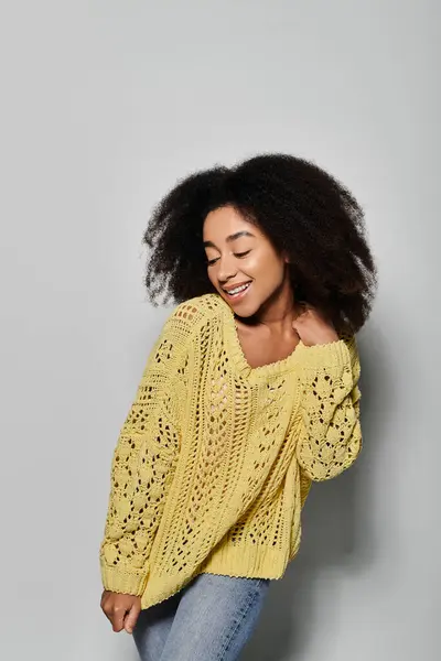 A young African American woman beams with joy, wearing a cozy yellow sweater in a studio setting. — Stock Photo