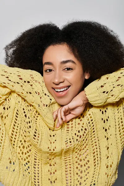 A joyful young woman with curly hair showcases her bright smile while wearing a cheerful yellow sweater. — Stock Photo