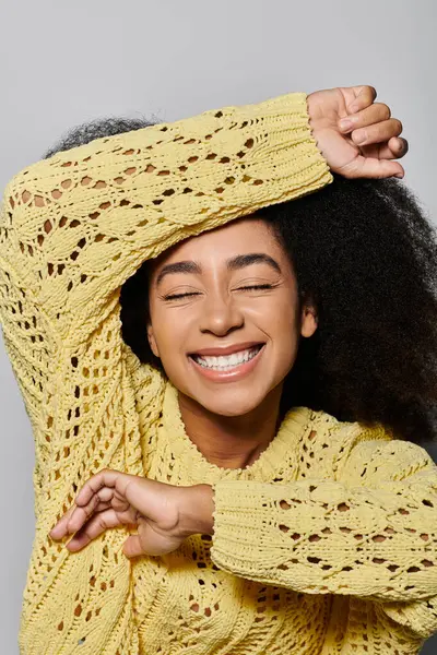 A cheerful young woman with curly hair beams with happiness in a bright yellow sweater. — Stock Photo