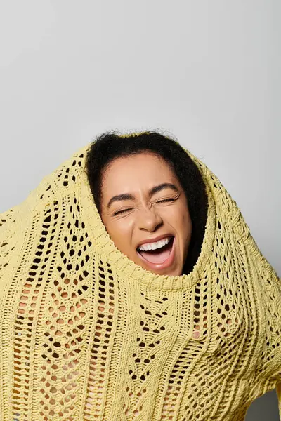 A joyful young woman bursts with laughter while playfully draping a yellow sweater over herself. — Stock Photo