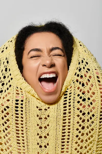A young woman bursts into laughter, her curly hair framed by a cheerful yellow sweater against a soft grey background. — Stock Photo