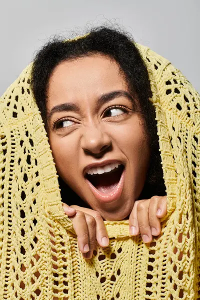 A young woman with curly hair joyfully reveals her face from a cozy yellow sweater. — Stock Photo
