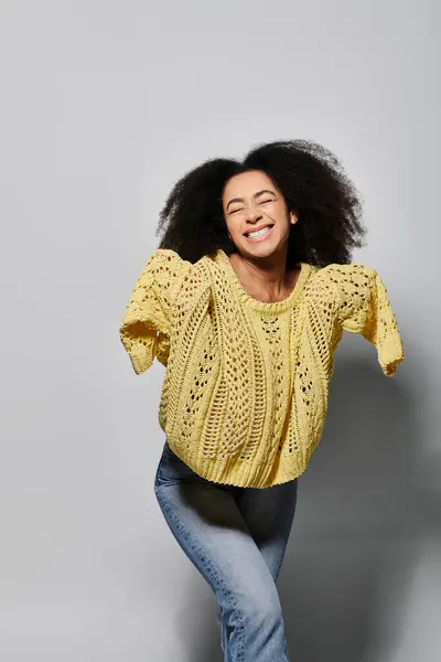 A cheerful young woman with curly hair radiates happiness while wearing a yellow sweater. — Stock Photo