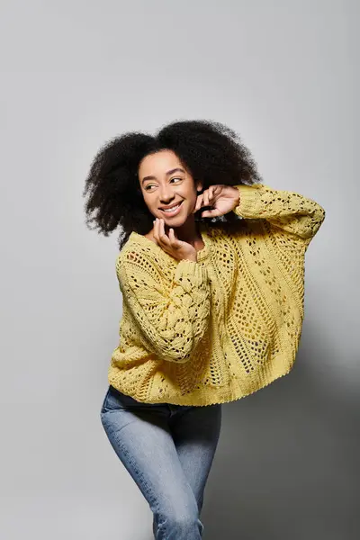 Eine junge Frau mit lockigem Haar lächelt freundlich, während sie einen gemütlichen gelben Pullover trägt. — Stockfoto