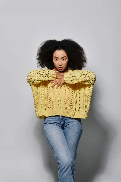 A young woman with curly hair showcases her style in a cozy yellow sweater, exuding confidence. — Stock Photo