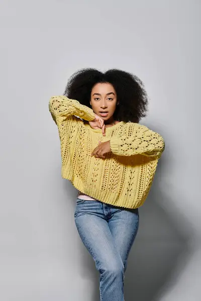 A young woman showcases her style with curly hair and a vibrant yellow sweater in a studio setting. — Stock Photo