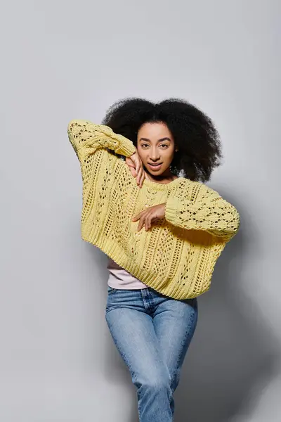 A young woman with curly hair showcases her vibrant yellow sweater in a creative studio setting. — Stock Photo