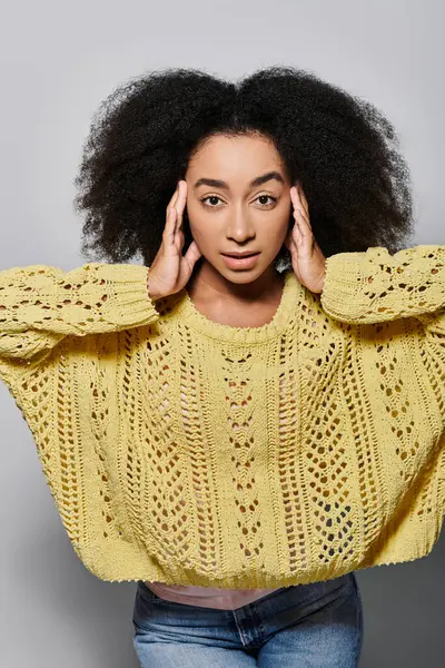 A young woman with curly hair gazes with intent while wearing a vibrant yellow sweater. — Stock Photo