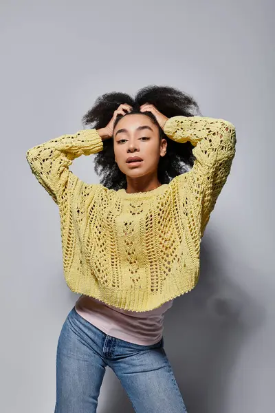 Une jeune femme affiche son style et son équilibre dans un pull jaune, sur un fond gris élégant. — Stock Photo