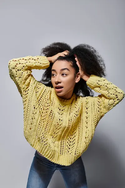 Una giovane donna con i capelli ricci mostra energia vibrante nel suo maglione giallo, coinvolgendo lo spettatore con la sua espressione.. — Foto stock