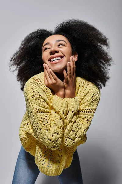 A young woman beams joyfully, showcasing her playful spirit in a bright yellow sweater against a grey backdrop. — Stock Photo