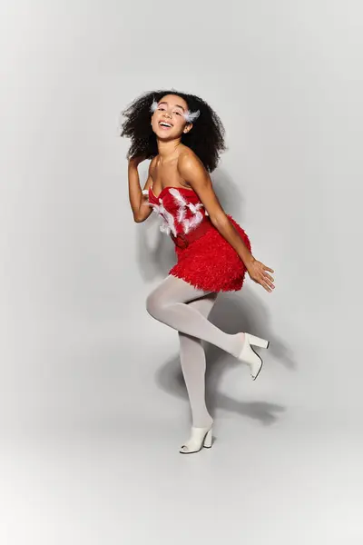 A young woman with curly hair gracefully poses in a striking red ensemble, showcasing her playful spirit. — Stock Photo