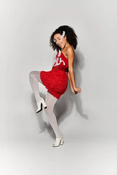 A vibrant young woman with curly hair shows off her red ensemble, striking a joyful pose in front of a grey backdrop. — Stock Photo