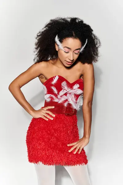 Une jeune femme met en valeur son style dans une tenue rouge audacieuse ornée de plumes, frappant une pose captivante. — Photo de stock