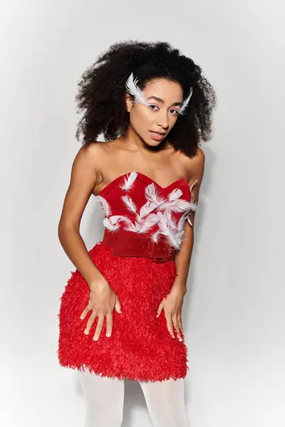 A young woman showcases her vibrant red outfit with feathers, exuding confidence against a grey background. — Stock Photo