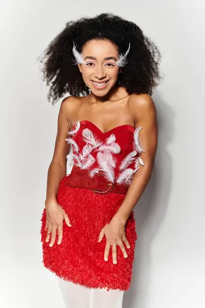 A young woman with curly hair showcases her style in a striking red ensemble adorned with feathers. — Stock Photo