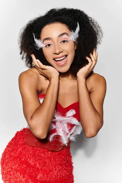A joyful young woman with curly hair showcases her red feathered attire while smiling brightly. — Stock Photo