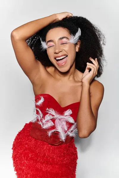 A young woman with curly hair beams joyfully while showcasing her striking red feathered outfit. — Stock Photo