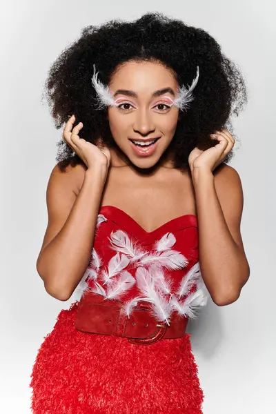 A vibrant young woman expresses joy while showcasing her stylish red feathered ensemble against a neutral background. — Stock Photo
