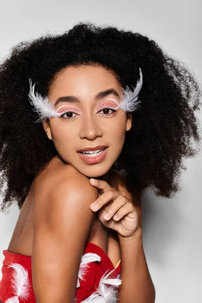 A stylish young woman with curly hair showcases her bold red outfit featuring feathers, exuding confidence. — Stock Photo