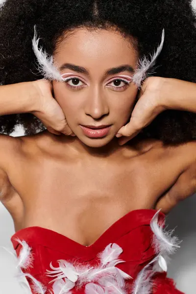 A young woman poses confidently in a red outfit adorned with feathers against a striking grey background. — Stock Photo