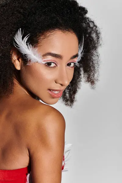 A young woman showcases her curly hair and striking red outfit, adorned with feathers, exuding confidence. — Stock Photo