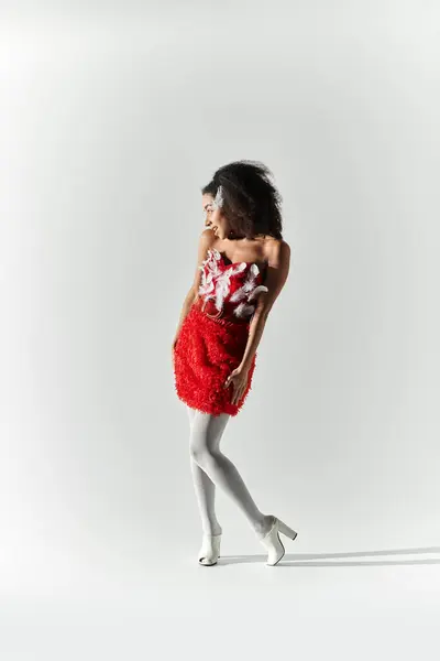 A young woman twirls playfully, showcasing her stylish red outfit with feathers on a simple grey background. — Stock Photo
