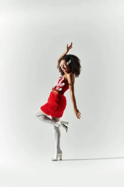 A young woman with curly hair elegantly poses in a vibrant red outfit, exuding confidence and style. — Stock Photo