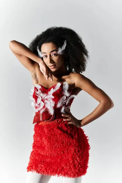 Une jeune femme aux cheveux bouclés pose en toute confiance dans une tenue rouge vif ornée de plumes. — Photo de stock