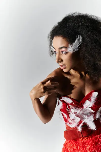 A young woman exudes confidence in a vibrant red outfit adorned with feathers, showcasing elegance. — Stock Photo
