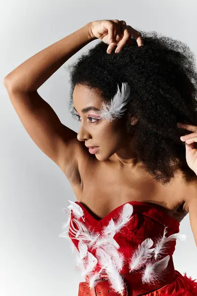 A young woman poses confidently in a striking red outfit adorned with feathers against a grey backdrop. — Stock Photo