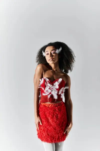 A confident young woman poses gracefully in a striking red outfit adorned with feathers. — Stock Photo