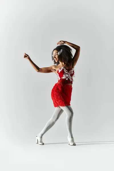 A young woman dances gracefully in a striking red feathered outfit on a neutral grey backdrop. — Stock Photo